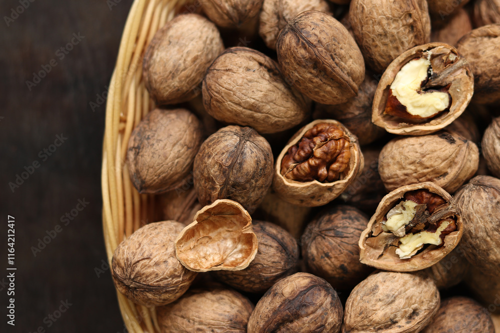 Walnuts in a wicker basket on a dark wooden background. Nuts in an oval basket, top view. Heap of walnuts in shells, close-up, background. Healthy eating. Harvest, agriculture Walnuts in a wicker basket on a dark wooden background. Nuts in an oval basket, top view. Heap of walnuts in shells, close-up, background. Healthy eating. Harvest, agriculture