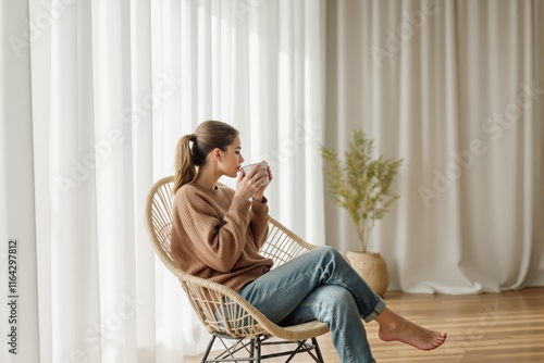 Woman sitting on a chair, drinking coffee in a cozy room with white curtains and wooden flooring. photo