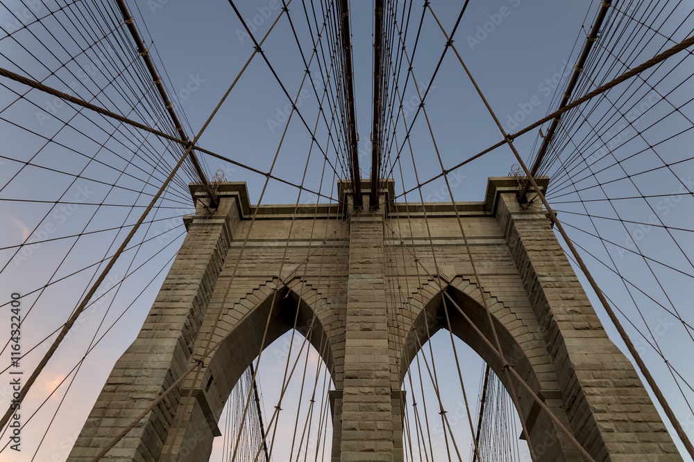 Naklejka premium Brooklyn Bridge close up detail looking up at suspension cables at sunrise (beautiful landmark travel tourism destination in NYC) iconic New York City attraction over east river downtown Manhattan USA
