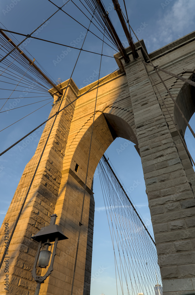 Naklejka premium Brooklyn Bridge close up detail looking up at suspension cables at sunrise (beautiful landmark travel tourism destination in NYC) iconic New York City attraction over east river downtown Manhattan USA