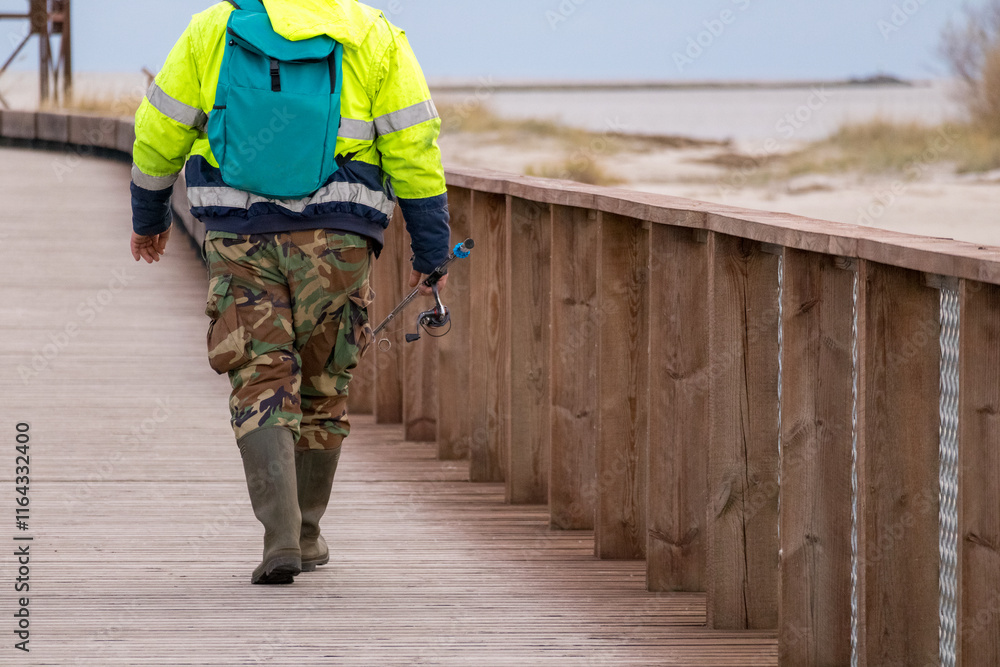 An angler with a spinning wheel in his hands walks along the boardwalk in rubber boots
An angler with a spinning wheel in his hands walks along the boardwalk in rubber boots