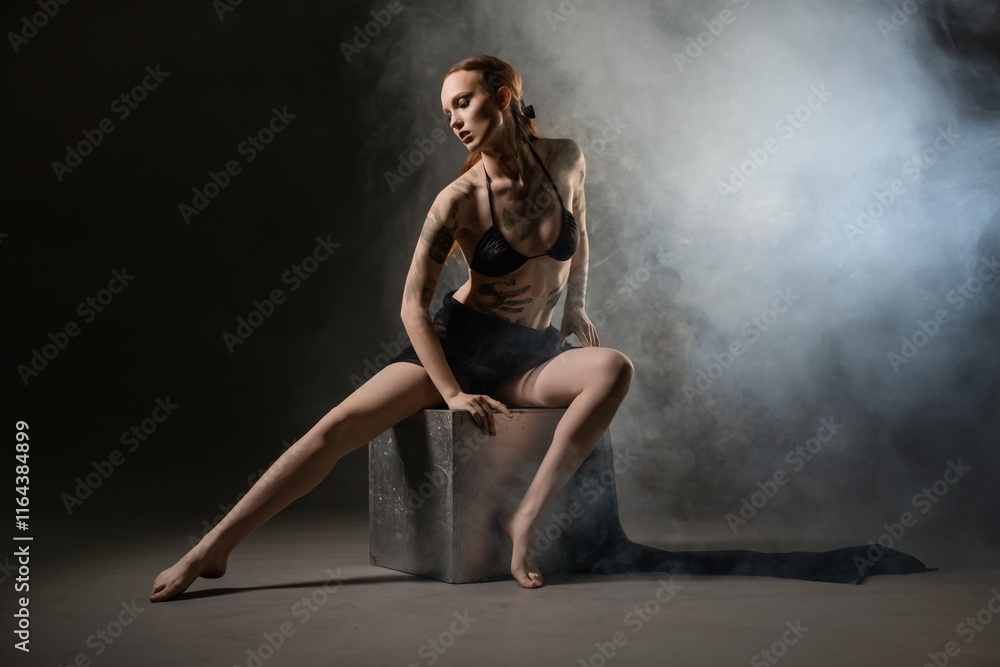 Dancer poses on a cube in a smoky studio during evening performance Dancer poses on a cube in a smoky studio during evening performance
