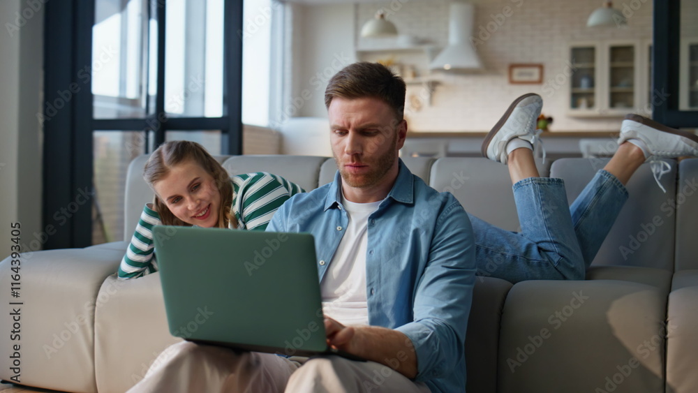 Focused boyfriend working laptop girlfriend leaning at sofa. Man solving tasks Focused boyfriend working laptop girlfriend leaning at sofa. Man solving tasks