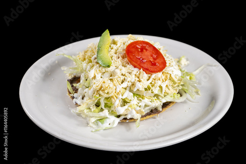 Chicken tostada with beans, lettuce, tomatoes, avocado in a white dish
