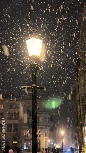 It is snowing against the background of the night sky and a beautiful glowing old street lamp in winter. Night shot. Vertical video.