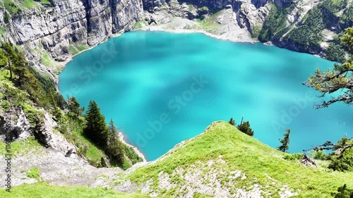 Slow drone flight above grassy cliffs high above the Oeschinensee lake in the  Swiss Alps. Down view towards the turquoise blue lake. Beautiful Swiss mountains, amazing nature. Outdoor adventure, heal