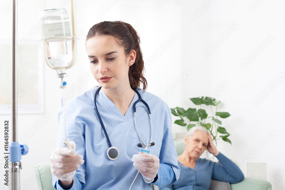 Young friendly nurse or doctor help sick senior elderly woman patient in receiving IV drip infusion and vitamin injection therapy sitting on sofa in medical clinic or at home. Health care concept Young friendly nurse or doctor help sick senior elderly woman patient in receiving IV drip infusion and vitamin injection therapy sitting on sofa in medical clinic or at home. Health care concept