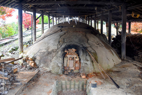 A traditional Japanese noborigama kiln, used for porcelain making, surrounded by rustic wooden beams and vibrant autumn trees, reflecting craftsmanship and history in pottery.
