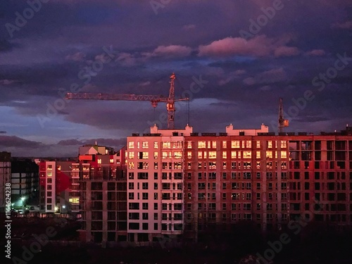 Tower cranes on the construction of a building with a frame of reinforced concrete, building on sunset background, view of the city.