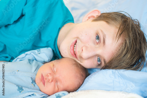 12 year old boy hugs his sleeping newborn brother. Happy teenager lies with his baby brother on the bed.