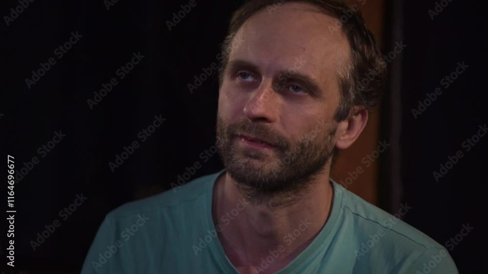 A man gazes upwards with a bored and slightly weary expression, his head resting on his hand. The simple background and indoor setting contribute to the overall mood A man gazes upwards with a bored and slightly weary expression, his head resting on his hand. The simple background and indoor setting contribute to the overall mood