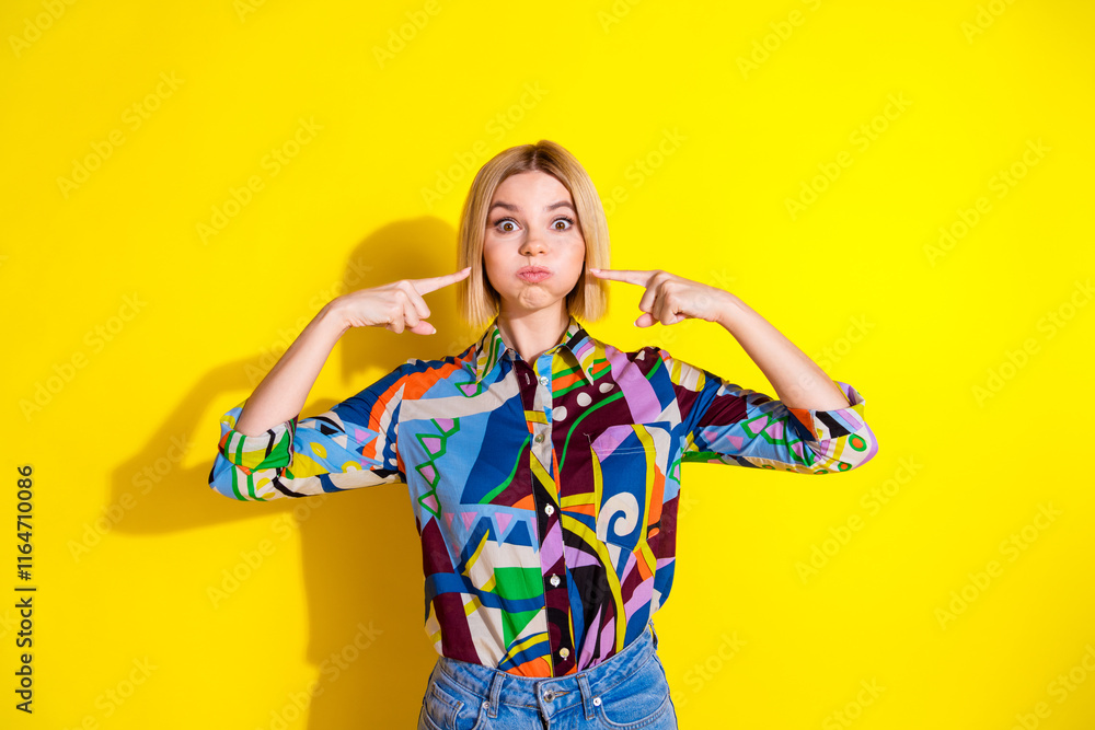 Photo portrait of pretty young girl hold breath blow cheeks point wear trendy colorful outfit isolated on yellow color background Photo portrait of pretty young girl hold breath blow cheeks point wear trendy colorful outfit isolated on yellow color background