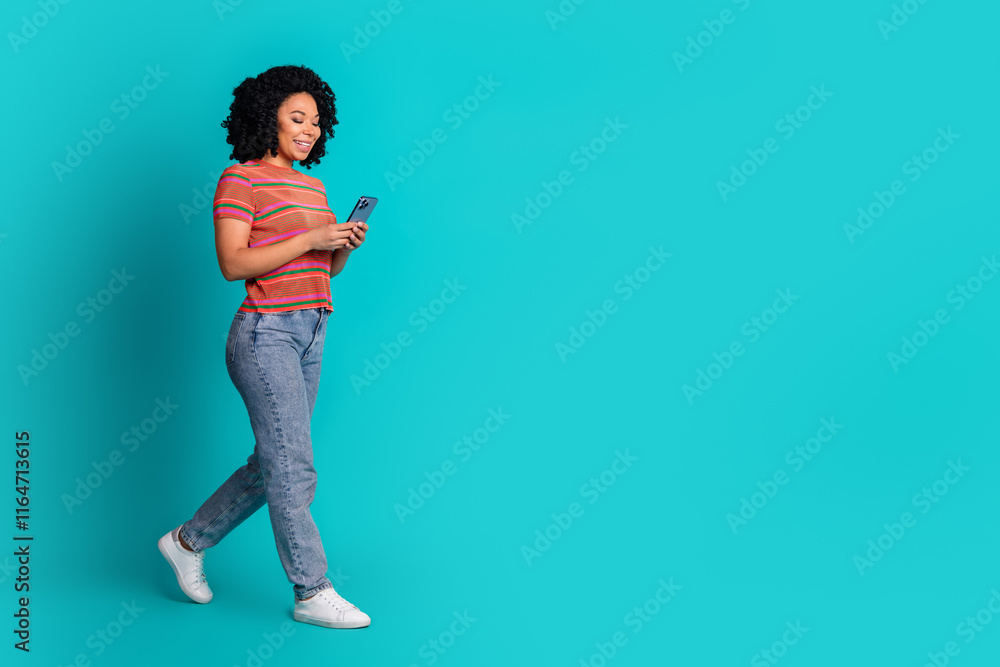 Full size photo of pretty young girl use phone walk empty space isolated on teal color background Full size photo of pretty young girl use phone walk empty space isolated on teal color background