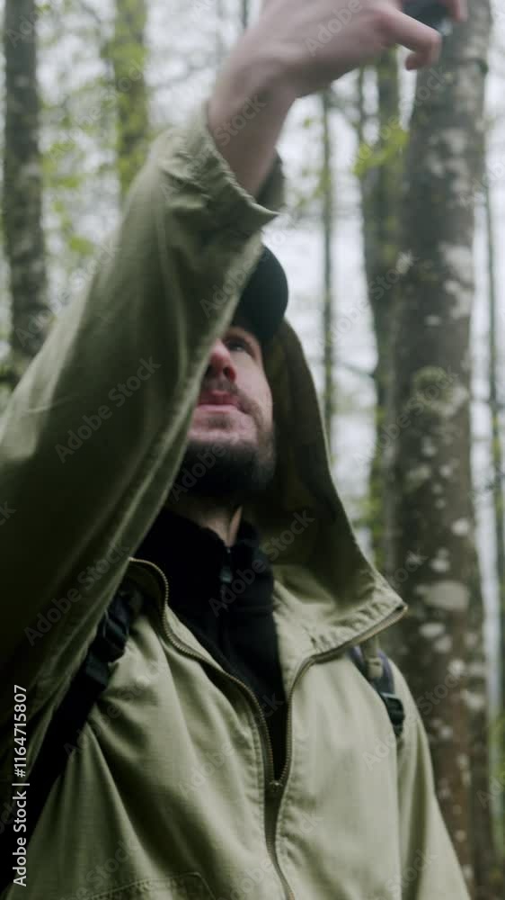 Vertical video. Worried male hiker with backpack lost in forest trying to find signal with mobile phone.	
