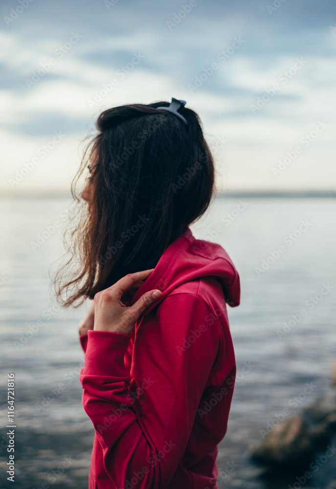 Side view of a woman with long hair wearing a hoodie standing by the sea Side view of a woman with long hair wearing a hoodie standing by the sea