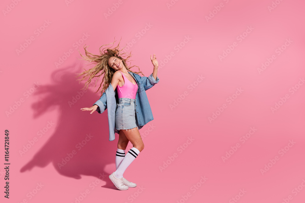 Vibrant young woman in denim and pink swaying happily against a lively pink background Vibrant young woman in denim and pink swaying happily against a lively pink background