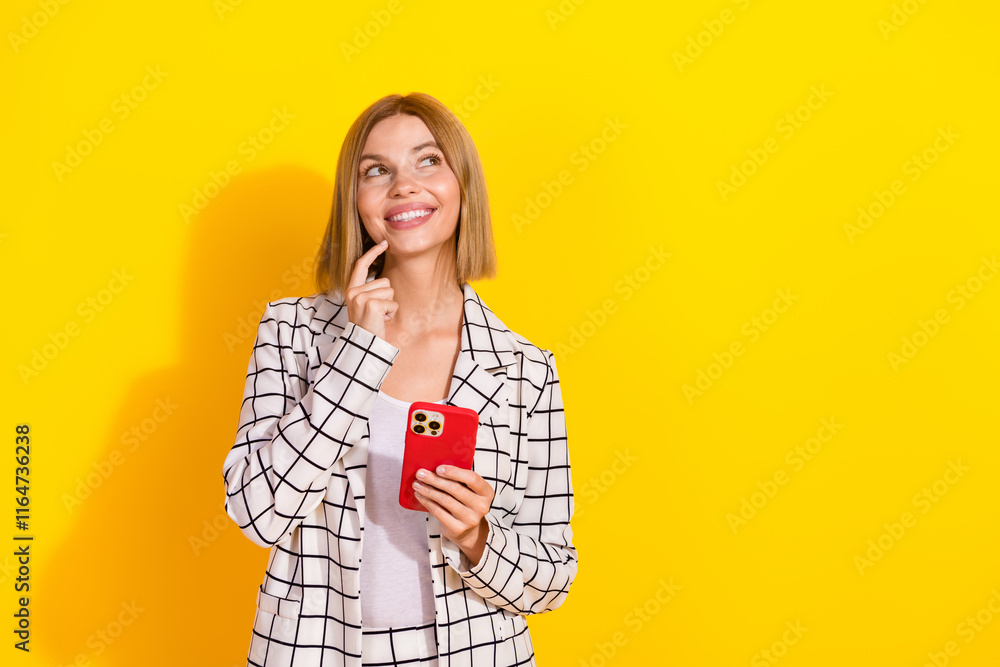 Young businesswoman in an elegant suit thinking about shopping ideas on her phone against a vibrant yellow background Young businesswoman in an elegant suit thinking about shopping ideas on her phone against a vibrant yellow background