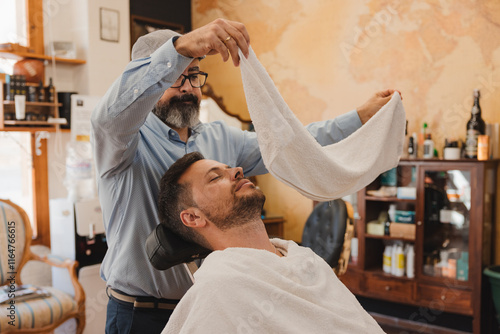 barbershop concept and people - Barber applies a hot towel to a man's beard.