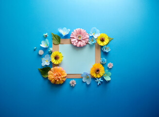 A blank card is surrounded by colorful flowers arranged on a vibrant blue background.  A spring or summer themed image, perfect for invitations or announcements.