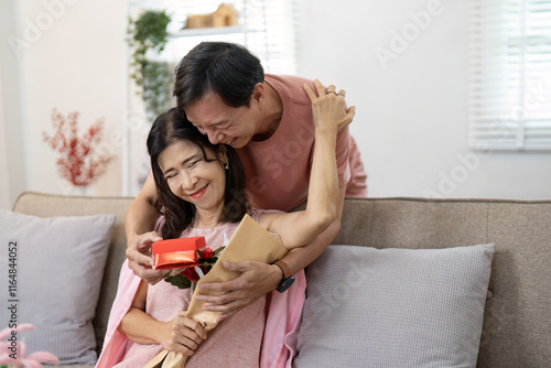 Elderly Couple Celebrating Valentine's Day with Gift Exchange and Affectionate Embrace in Cozy Home Setting photo