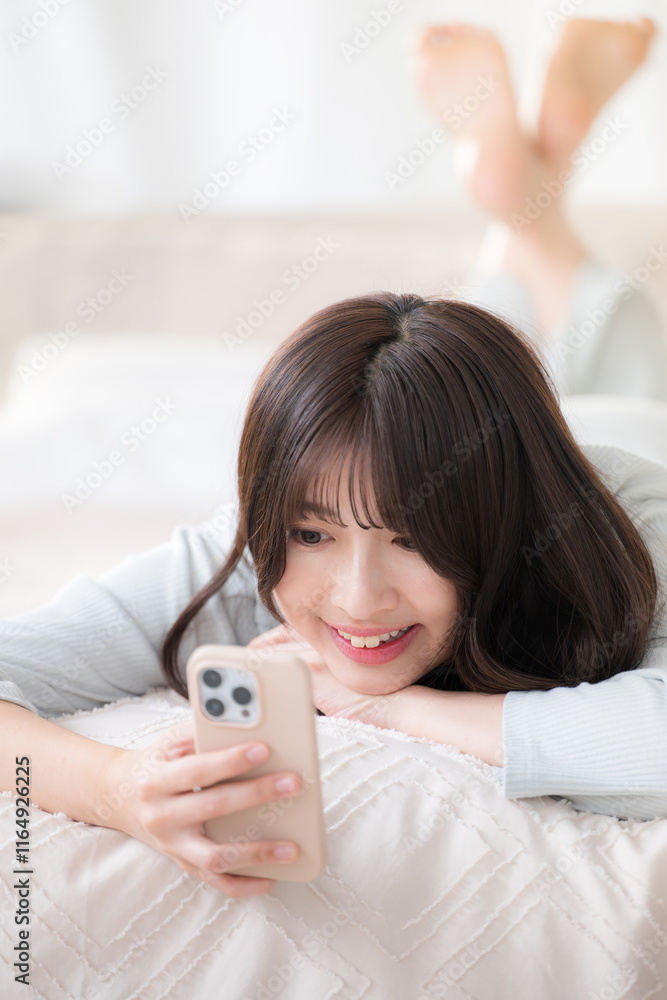 ベットで寝転がってスマホを見る笑顔の若いかわいい女性のクローズアップ ベットで寝転がってスマホを見る笑顔の若いかわいい女性のクローズアップ