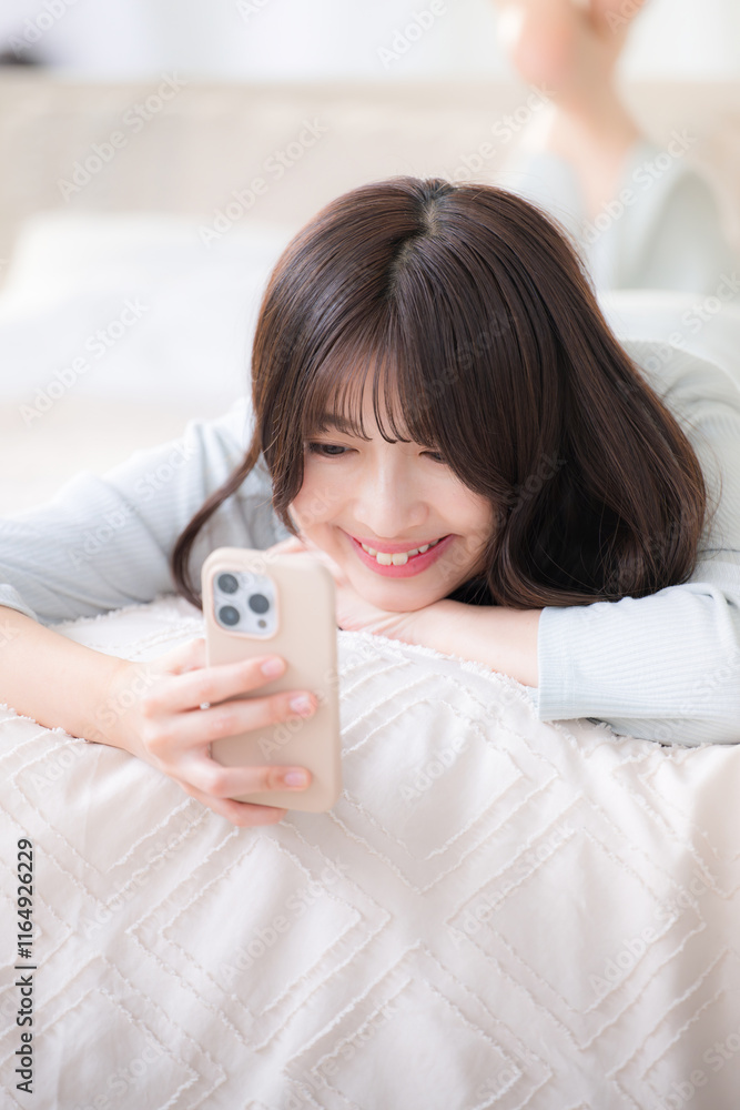 Close-up of a smiling young pretty woman lying on a bed looking at her phone,veritical