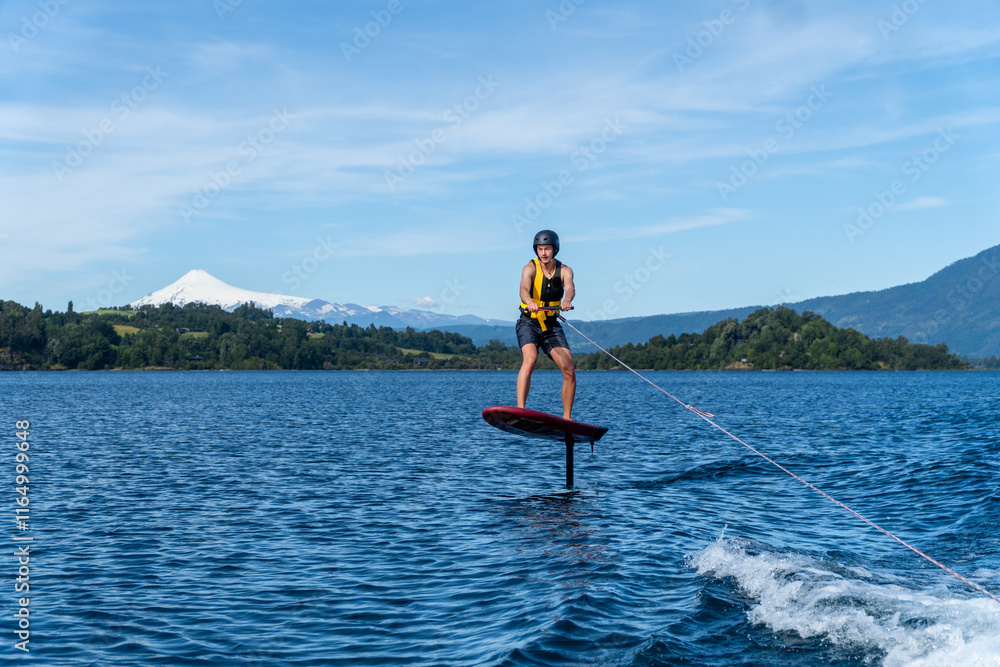 A young man glides on a foil board across the lake, surrounded by a breathtaking natural landscape.