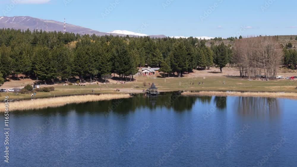 Tourists enjoying sunny day at la zeta lagoon, a beautiful natural reserve near esquel, patagonia, argentina, with the andes mountains reflecting on the calm water surface, drone establishing shot Tourists enjoying sunny day at la zeta lagoon, a beautiful natural reserve near esquel, patagonia, argentina, with the andes mountains reflecting on the calm water surface, drone establishing shot