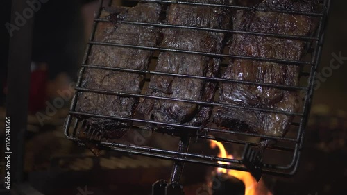 Grilling pieces of meat on a barbecue in patagonia, Argentina, with vibrant flames dancing below, creates an authentic and delicious culinary experience in the outdoors, slow motion reveal photo