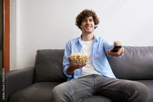 young handsome man watching movies and eating popcorn in a living room #1165145051