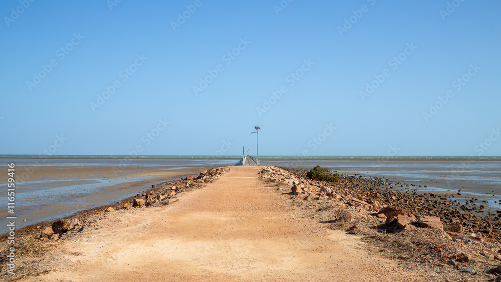 A perspective view of an earth and rock pier leading to a wooden historical pier that stretches off into the distance across a large tidal flat at Port Germein in South Australia. A perspective view of an earth and rock pier leading to a wooden historical pier that stretches off into the distance across a large tidal flat at Port Germein in South Australia.
