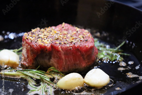 Seasoned filet steak searing with garlic and rosemary in a skillet
