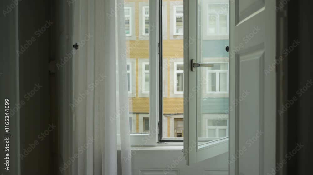 Open glass window in an apartment house or hotel suite overlooking the city street during daytime. Drapes open. Mysterious and eerie. Fresh air and wind coming in. Sign of break in or burglary scene Open glass window in an apartment house or hotel suite overlooking the city street during daytime. Drapes open. Mysterious and eerie. Fresh air and wind coming in. Sign of break in or burglary scene