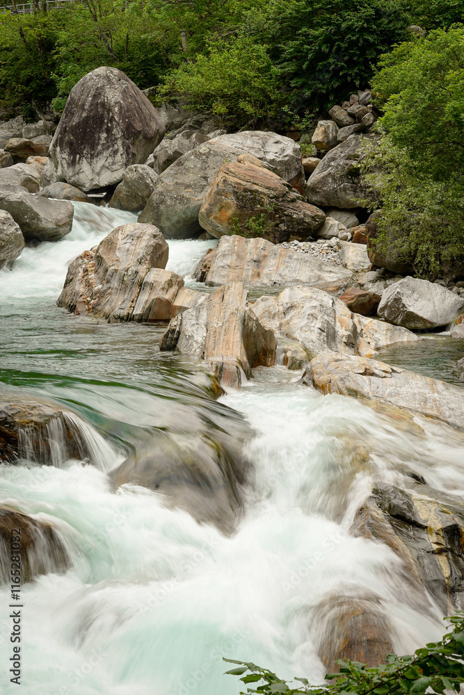 Motion blurred fast turquoise mountain river flowing thought big stones in a mountain valley in Switzerland Motion blurred fast turquoise mountain river flowing thought big stones in a mountain valley in Switzerland