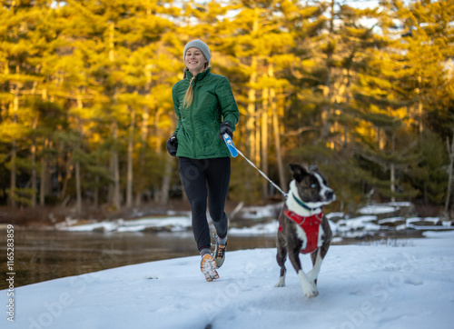 smiling woman runs with dog along snow covered trail in Maine photo