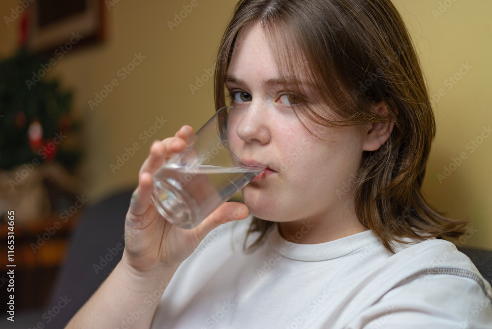 Girl drinking water sitting on a couch at home and looking at camera Girl drinking water sitting on a couch at home and looking at camera