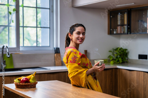 Young Indian asian girl in salwar kameez sipping coffee in sunlight in a modern kitchen photo