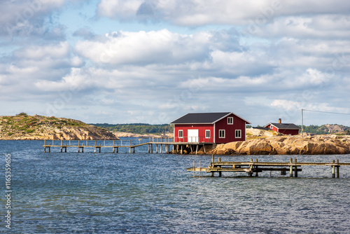 Seascape on the Resö island in the Bohuslän province, Sweden, showing a typical red painted boathouse on the rocky coast with a wooden pier under a stormy sky on a sunny summer day.