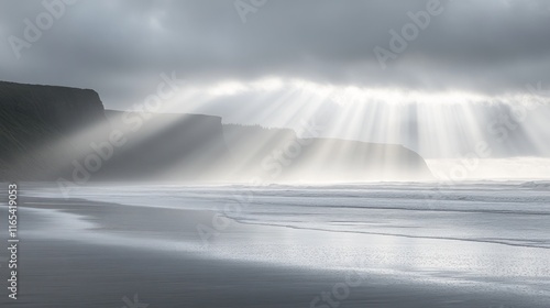 Dramatic coastal scene with sun rays breaking through overcast sky over a dark sand beach.