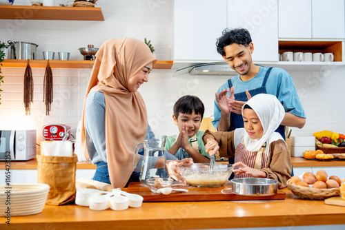Asian muslim father, mother and brother cheer up the girl to mix flour in the bowl and stay together in kitchen of their house.