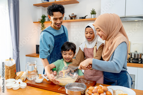 Wide shot of muslim family with father, mother, boy and girl enjoy to make the bakery with mix flour in bowl and stay together in kitchen with happiness.