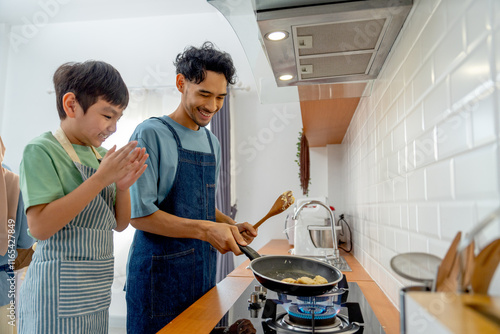 Young Asian father enjoy to teaching to make pan cake for his son who cheer up beside in the kitchen of their house. photo