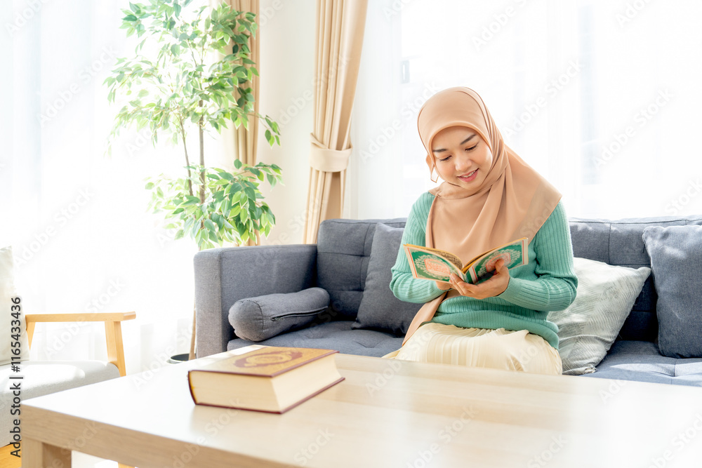 Wide shot of Asian beautiful muslim woman sit on sofa in her house and read the book relate to her religion and smile with happiness. Wide shot of Asian beautiful muslim woman sit on sofa in her house and read the book relate to her religion and smile with happiness.