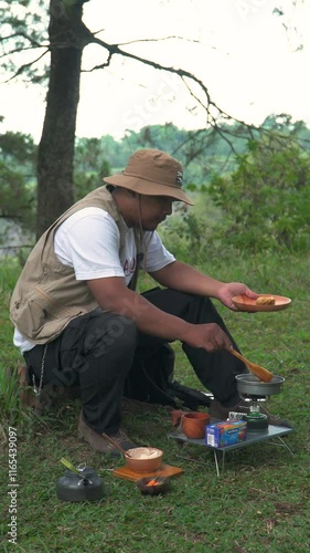 The Bushcraft concept cooks fried tempeh with soy sauce in a dense and green pine forest area. An Asian male solo adventurer is in the process of preparing and cooking in beautiful nature