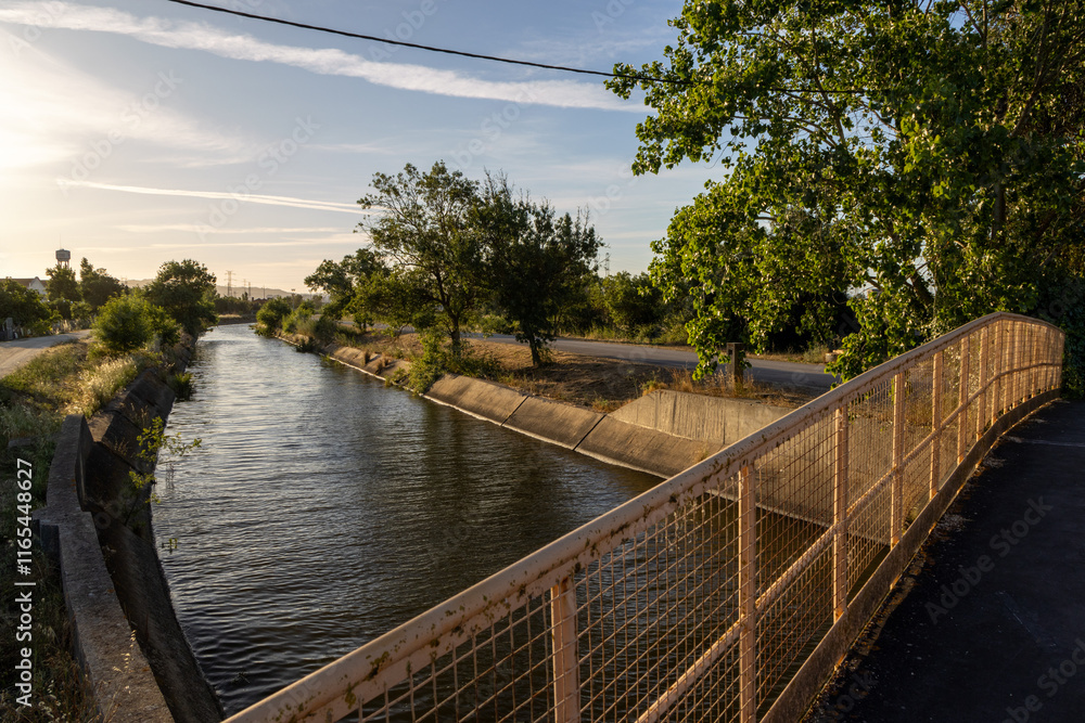 Fototapeta premium Irrigation canal flowing under bridge at sunset in the countryside