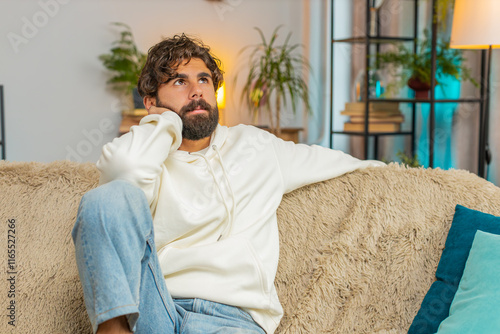 Sad lonely man sits at home room looks pensive thinks over life concerns or unrequited love suffers from unfair situation. Indian alone guy problem, break up, depressed feeling bad annoyed burnout. photo