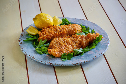 Фотография crispy fried fish fillets served on a blue plate with fresh lemon and parsley