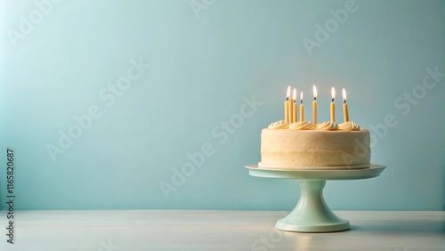 A single-tier vanilla cake with lit candles on a pastel green cake stand sits on a white wooden table against a light aqua background. photo