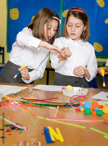 Elementary School: Sibling Rivalry. A pair of young primary school identical twin sisters working together on a class art project.