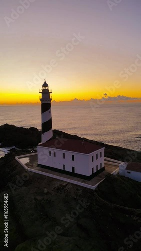 Dramatic Vertical Sunset Over Favaritx Lighthouse. Faro de Favaritx, Menorca, Spain - Iconic Landmark Amidst Golden Hour Skies and Serene Sea